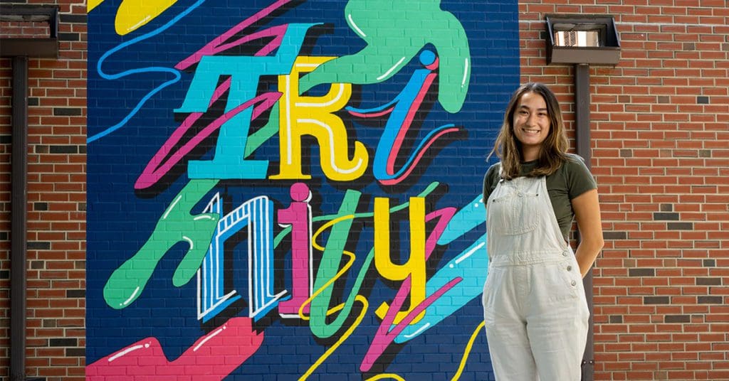 Yuri Coleman standing in front of her Trinity mural installment